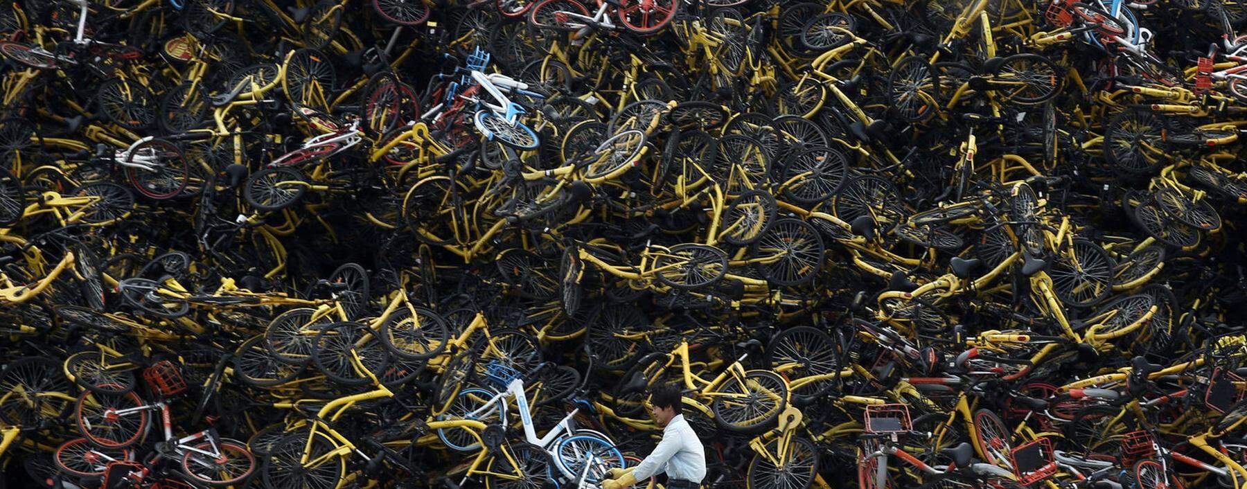 Worker rides a shared bicycle past piled-up shared bikes at a vacant lot in Xiamen