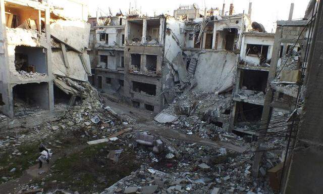 A man walks along a street lined with damaged buildings in the besieged area of Homs