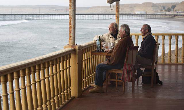Three male friends enjoy a drink and good conversation on colonial style balcony overlooking the oce