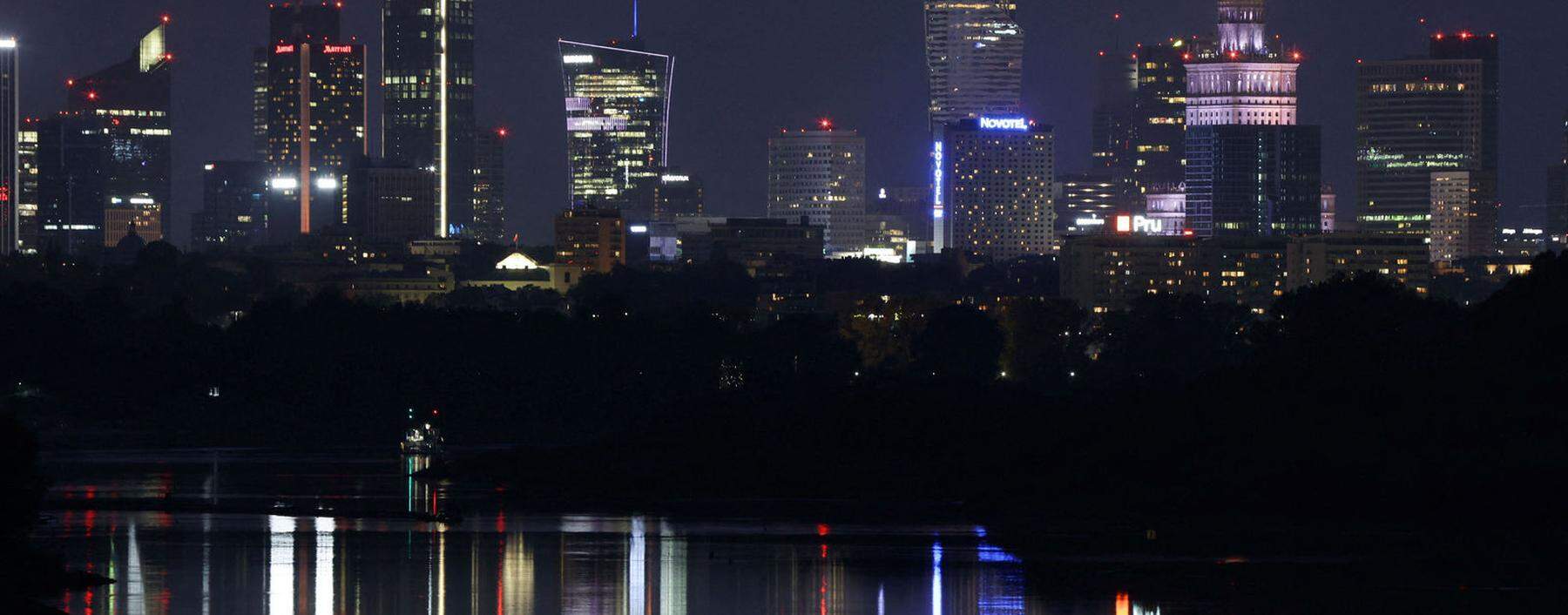 A skyline of skyscrapers is reflected in the Vistula river in the evening in Warsaw