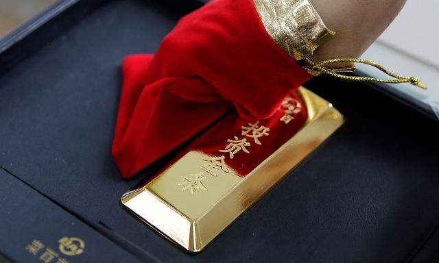 A sales assistant displays a 1000 gram gold bar as an investment for a customer at Caibai Jewelry store in Beijing