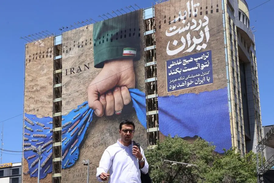 <strong>25. Mai. </strong>Ein Mann überquert auf dem Vanak-Platz in Teheran eine Straße und kommt dabei an einer Plakatwand an der Fassade eines Gebäudes vorbei, auf der die Straße von Hormus abgebildet ist. 