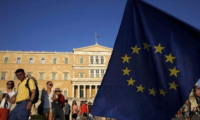 Tourists make their way past a European Union flag waved by a protester in front of the parliament building during a Pro-Euro rally in Athens