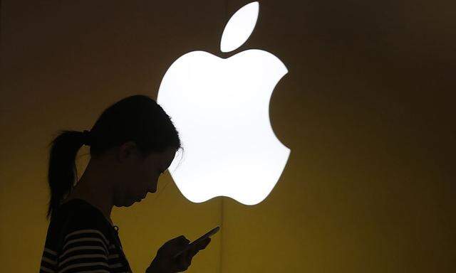 A woman looks at the screen of her mobile phone in front of an Apple logo outside an Apple store in downtown Shanghai