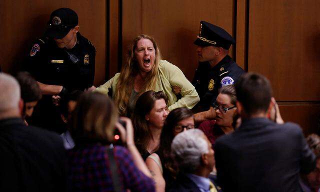 Eine Demonstrantin wird aus dem Anhörungssaal geführt.