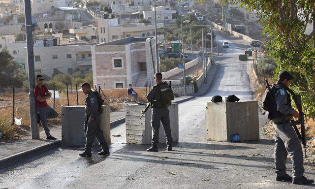 A Palestinian stands to the side of Israeli border police at a newly installed concrete block checkp