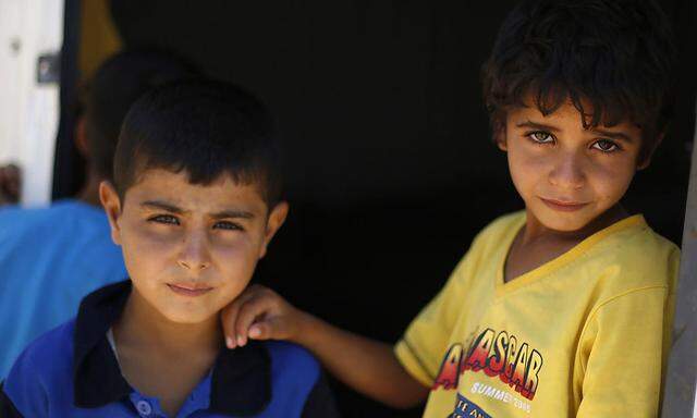 Syrian refugee children stand in front of their family residence at Azraq refugee camp