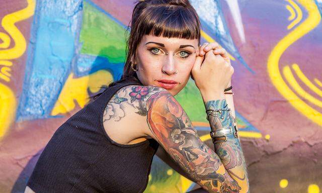 tattooed rebel girl posing against a wall