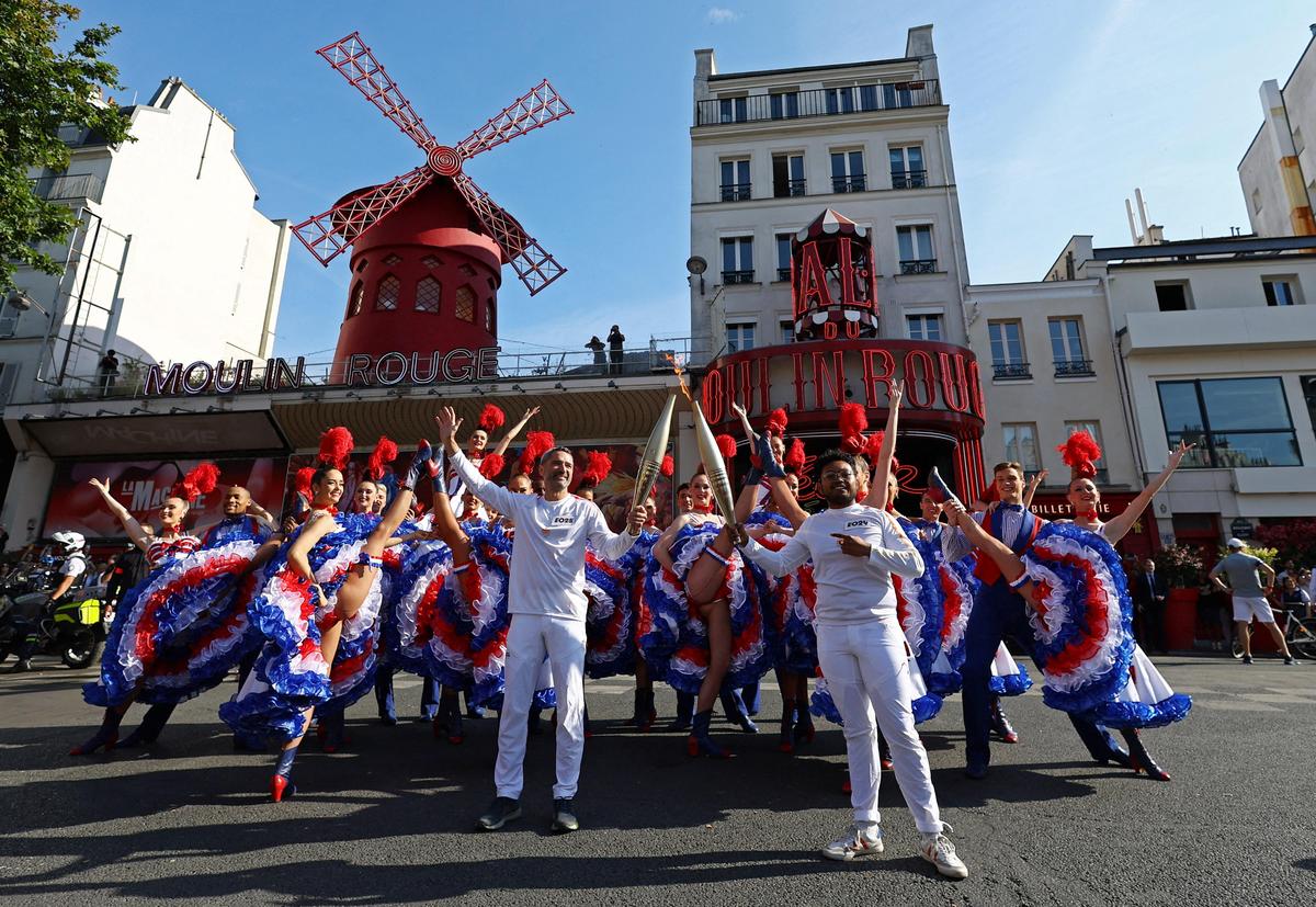 15. Juli. Die olympische Fackel passiert das legendäre Lokal „Moulin Rouge“ in Paris. 