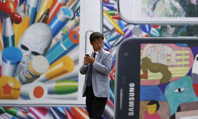 A man uses his mobile phone in front of a giant advertisement promoting Samsung Electronics´ new Galaxy S5 smartphone, at an art hall in central Seoul