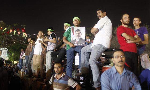 Supporter of Egypt's deposed President Mursi holds a poster of him while waiting with others during their sit-in outside the Rabaa Adawiya mosque, east of Cairo