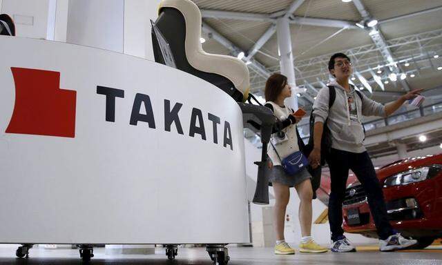 Visitors walk behind a logo of Takata Corp on its display at a showroom for vehicles in Tokyo