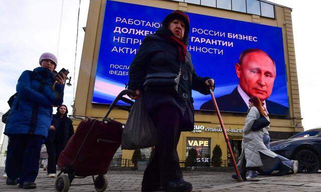 Passanten in St. Petersburg vor einem Infoscreen, auf dem Präsident Putin zu sehen ist, aufgenommen am 13. März 2024. 