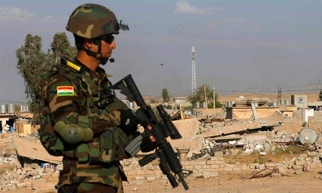 Ein kurdischer Kämpfer vor einem durch Luftangriffe zerstörtem Haus.