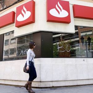A woman walks past the vandalized windows of a Banco Santander branch in Valencia