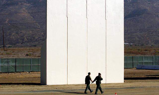 U.S. border patrol officers walk near a prototype for U.S. President Trump´s border wall with Mexico, in this picture taken from the Mexican side of the border, in Tijuana