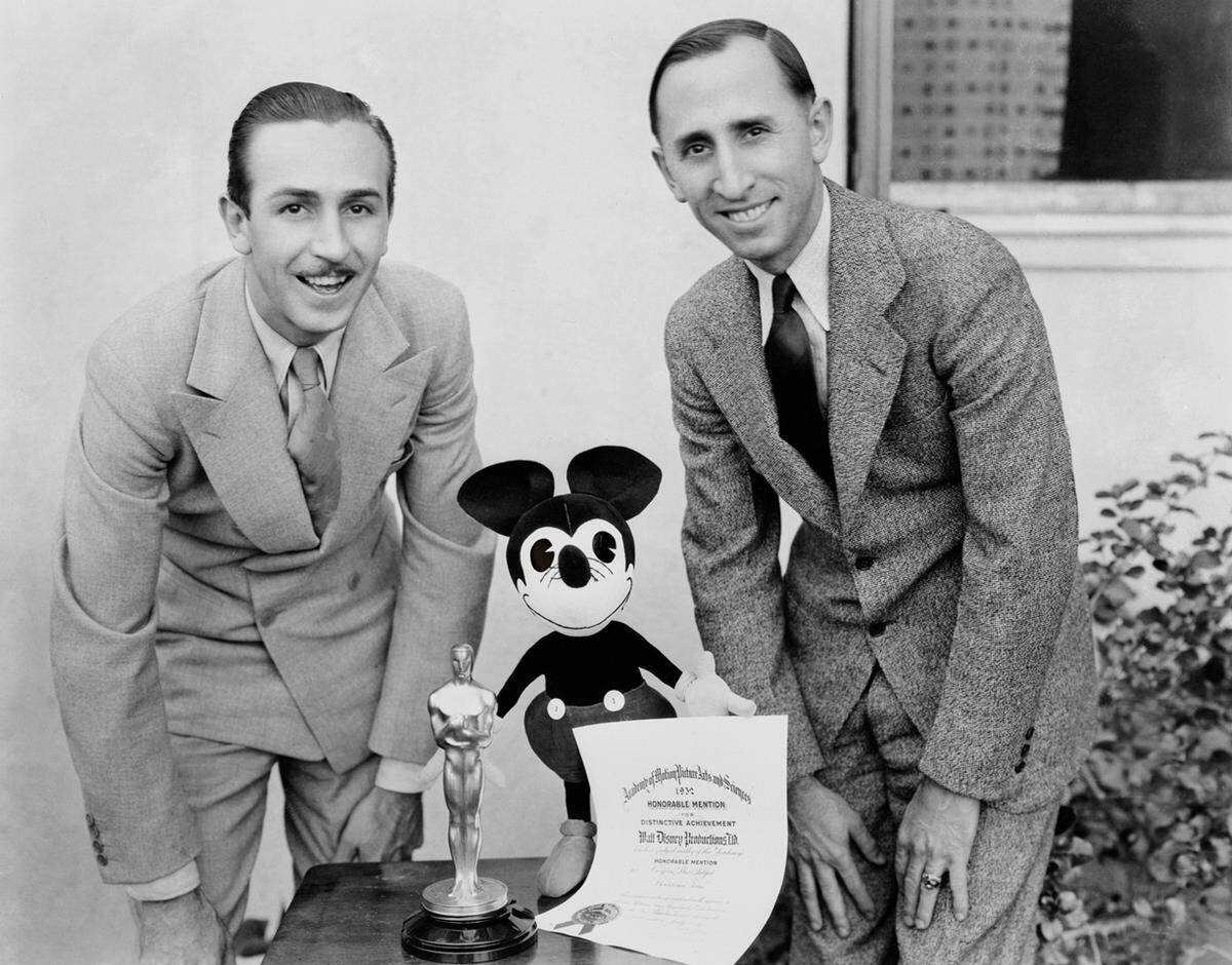 Die Mäusefigur mit der übergroßen schwarzen Nase und den runden Ohren wurde aber rasch braver - und zur populärsten Zeichentrickfigur aller Zeiten. Als Symbol für Spaß und Optimismus wurde er mit der Zeit mit seinem Schöper Walt Disney gleichgesetzt. Und dieser mit seiner Figur. Im Bild: Walt Disney, sein Bruder Roy und Micky posieren 1932 mit dem Academy Award.