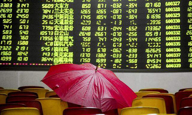 A red umbrella is placed on seats in front of an electronic board showing stock information at a brokerage house in Dongguan
