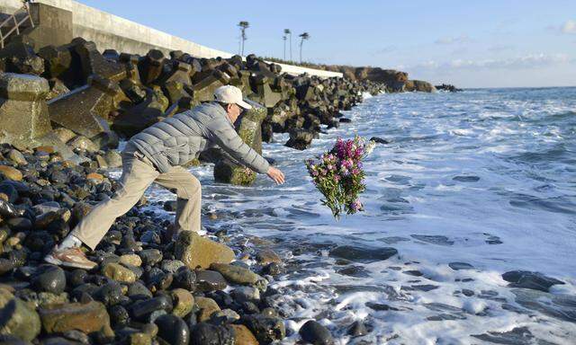 5 years since quake tsunami nuclear disasters A man throws a flower bouquet into the ocean in the