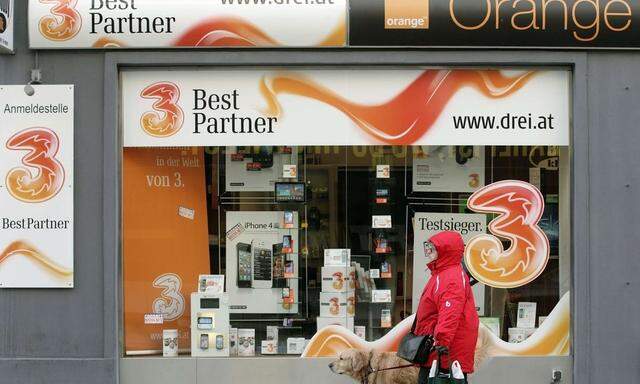 A woman and her dog walk by a telecommunications store advertising 'Orange' and '3' in Vienna