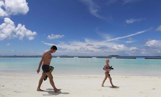 Touristen spazieren einen Strand auf einer der maledivischen Urlaubsinseln entlang.