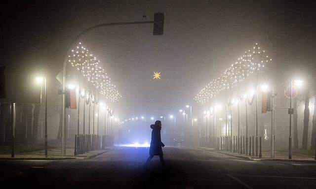 Eine Frau laeuft entlang einer mit Weihnachtsbeleuchtung geschmueckten Strasse im Nebel in Niesky, 11.12.2020. Die saech