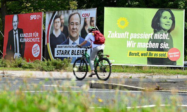 Radfahrerin fährt an Wahlplakaten mit den Spitzenkandidaten Olaf Scholz (SPD), Armin Laschet (CDU) und Annalena Baerbock (Bündnis 90/Die Grünen) vorbei. 