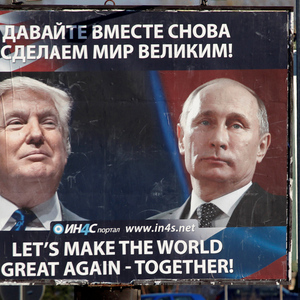 Pedestrians cross the street behind a billboard showing a pictures of Trump and Putin in Danilovgrad