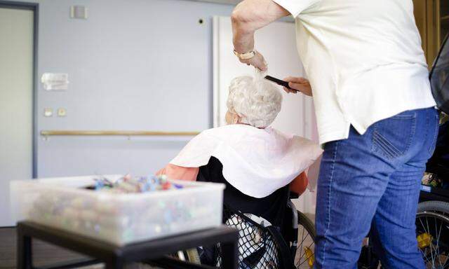 Eine Friseurin friesiert eine alte Frau im Rollstuhl in einem Pflegeheim, 27.04.2018, Berlin. NUR ZUR REDAKTIONELLEN VE