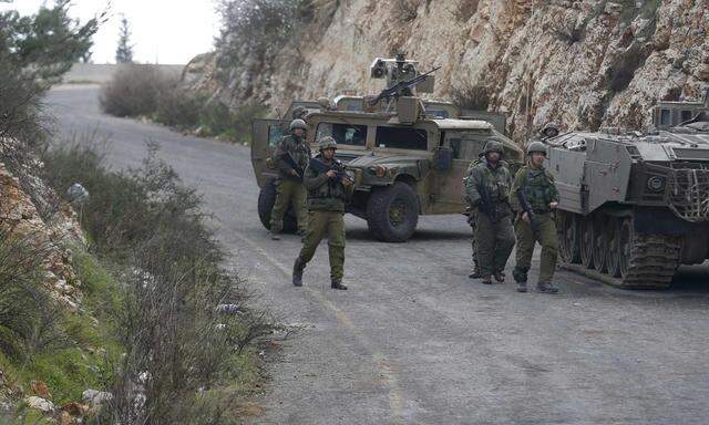 Israeli soldiers walk near military vehicles near Israel's border with Lebanon