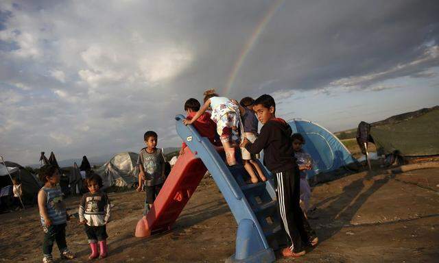 Children play on a slide as a rainbow forms overhead at a makeshift camp for refugees and migrants near the village of Idomeni