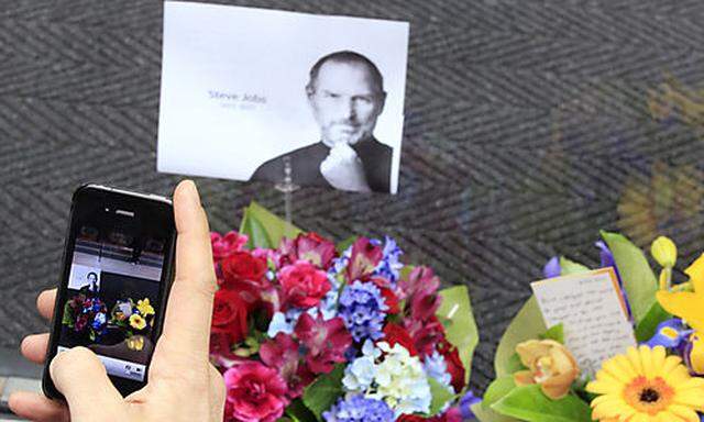 A man uses his iPhone to photograph flowers and a photocopy image of Steve Jobs that is placed at the