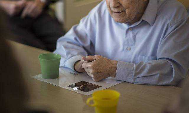 Ein alter Mann sitzt in einem Pflegeheim an einem Tisch Neben ihm steht ein Plastikbecher aufgeno