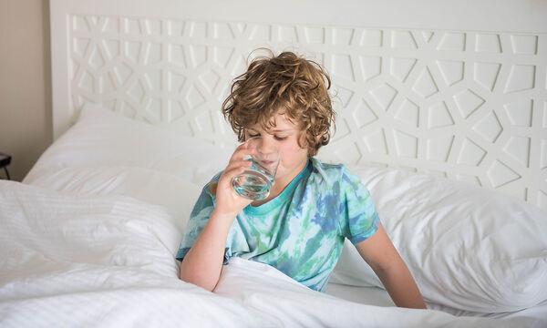 Young child sits in bed sick while trying to rest
