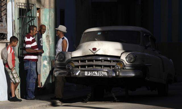Cubans talk near a broken car in Havana
