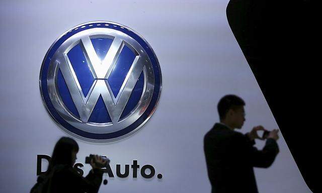 Guests stand next to a Volkswagen logo at the stage of the company at the 16th Shanghai International Automobile Industry Exhibition in Shanghai