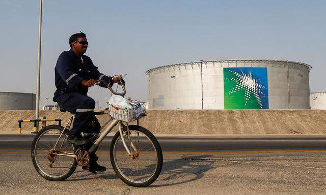 FILE PHOTO: An employee rides a bicycle next to oil tanks at Saudi Aramco oil facility in Abqaiq