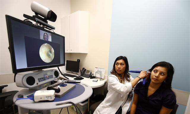 Nurse looks inside the ear of patient as doctor remotely views the procedure on a video screen at a newly opened Kaiser Permanente health clinic inside a Target retail department store in San Diego