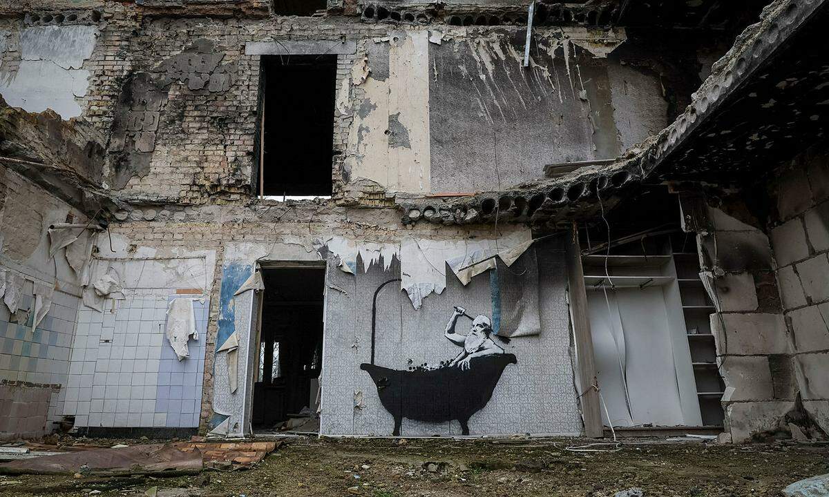 In Horenka bei Kiew sprühte er auf die geflieste Badezimmerwand eines zerstörtes Hauses das Bild eines Mannes in einer Badewanne, der sich den Rücken mit einer großen Bürste schrubbt.