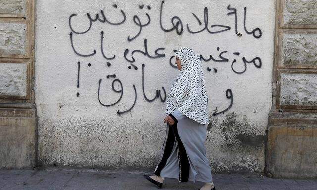 A woman walks past graffiti in Tunis