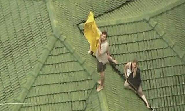 A man holds up a shirt on the roof of a house in Toowoomba