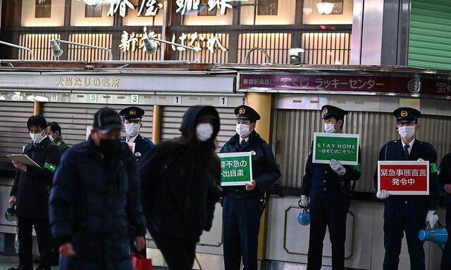 Polizisten weisen in Tokio Passanten darauf hin, wegen der Corona-Pandemie wenn möglich zu Hause zu bleiben.