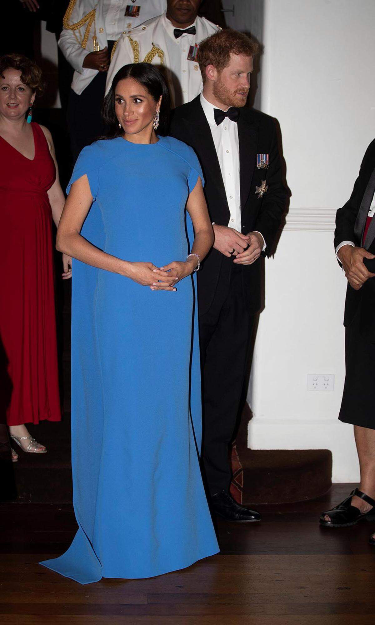 Später am Abend wechselte Herzogin Meghan noch einmal ihre Garderobe und zog bei ihrem ersten Staatsbankett in einem bodenlangen blauen (der Farbton soll das Blau in der Fahne des Inselstaates wiederspiegeln) Cape-Kleid des Labels Safiyaa alle Blicke auf sich.