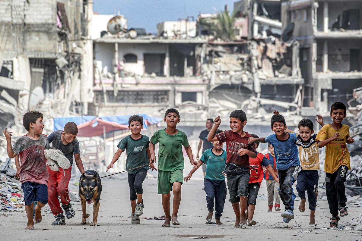 8. Juli. Kinder gehen mit einem Hund an zerstörten Gebäuden in einer Straße in Khan Yunis im südlichen Gazastreifen vorbei.