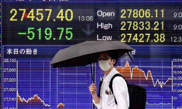 August 16, 2021, Tokyo, Japan: A man holding an umbrella walks in front of an electric board showing Nikkei index a brok