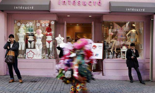 People use their mobile phones as they stand in front of a lingerie shop at a shopping district in Tokyo