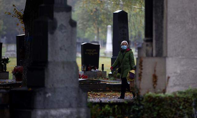 A woman wearing a protective face mask walks between tombstones at the Zentralfriedhof cemetery on an autumn day ahead of All Saints Day in Vienna