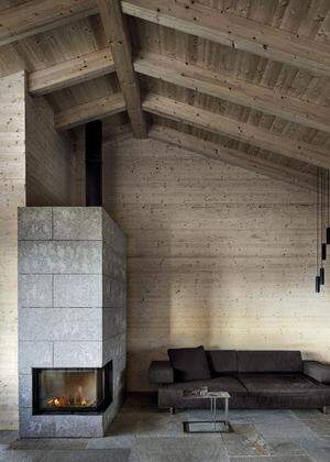 Blick in den Wohnbereich mit Steinboden, Fichtenholz an Wänden und Decke und Kamin.