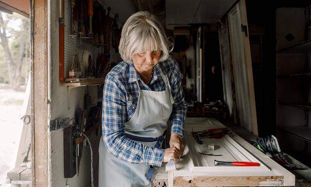 Confident senior female owner scraping on window frame at store workshop , model released, property released Copyright: