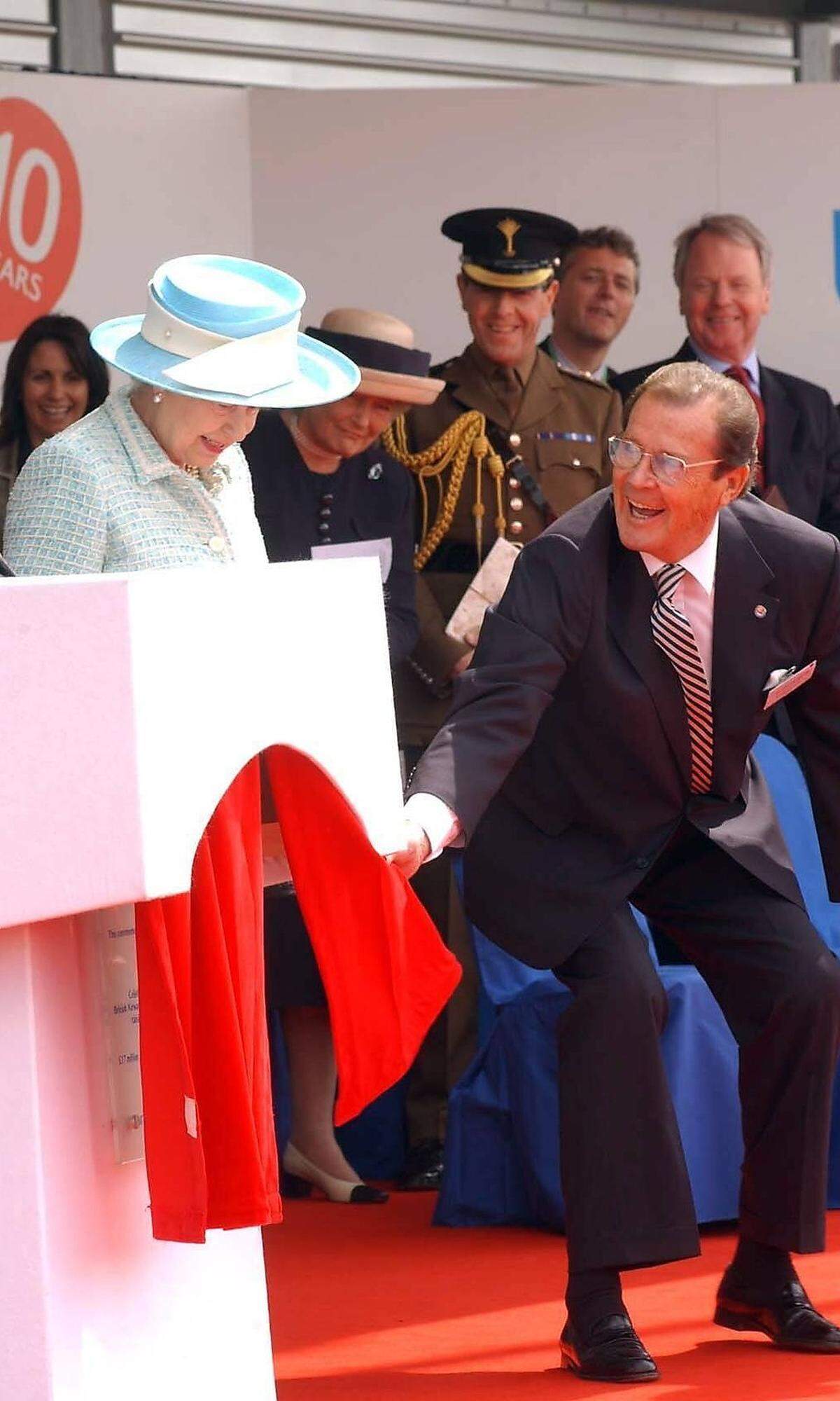 Für seinen Einsatz für Kinder erhielt Moore im Jahr 2003 in Deutschland des Bundesverdienstkreuz. Im selben jahr wurde er in seiner britischen Heimat in den Adelsstand erhoben. Bild: Sir Roger Moore hilft Queen Elizabeth II im Jahr 2004 nach ihrer Rede zum Anlass des 10-jährigen Bestehens einer Partnerschaft von Unicef und British Airways in London vom Podium.  